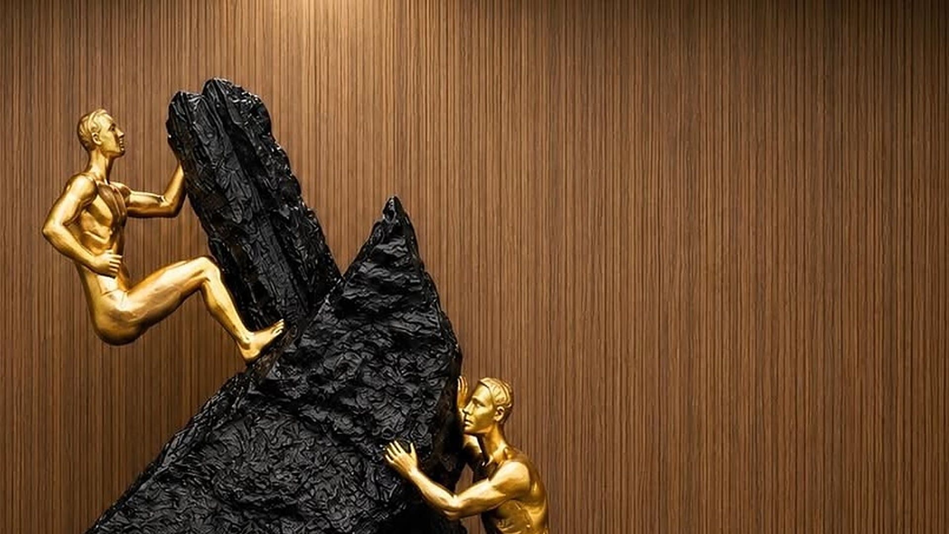 Gold climbers sculpture against a walnut wall